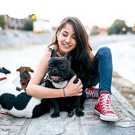 young woman with brown hair and red Converse shoes wraps an arm around a small black and white French bulldog