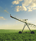 specially designed watering equipment sits on a farm field under a cloud-dotted blue sky
