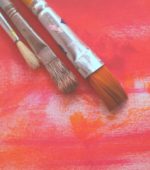three paintbrushes resting on a canvas with warm colors