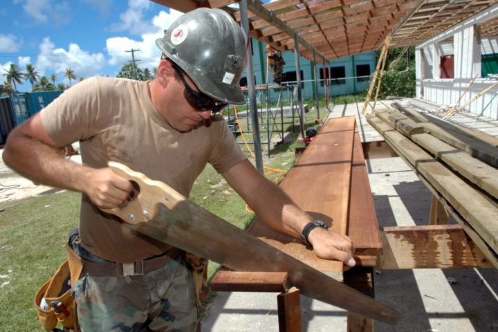 carpenter in hard hat sawing wood