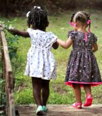two young preschool friends hold hands while crossing a bridge