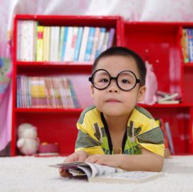 young child with glasses lays on floor reading book