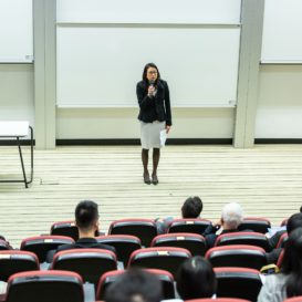 college professor holding microphone addresses large lecture hall
