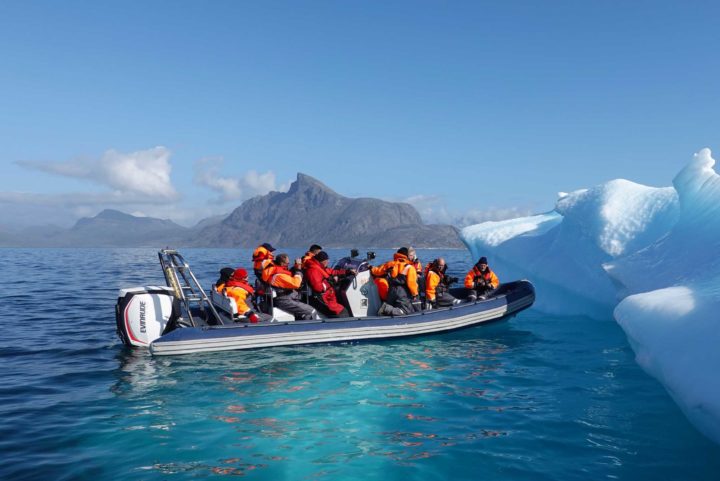 Group of Industrial Ecologists on a small boat aquiring samples from iceberg in bright blue water