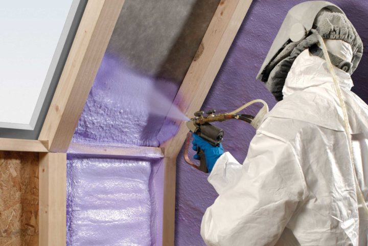 Weatherization technician applying purple insulation foam between 2x4s inside home