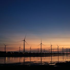 line of wind turbines generating clean energy against a blue and peach sunset
