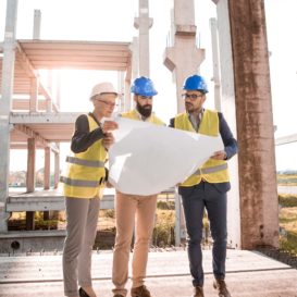 three architects reviewing blueprints on building site