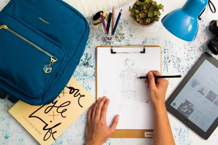 Fashion designer sketches a dress on a desk with lamp and tablet nearby