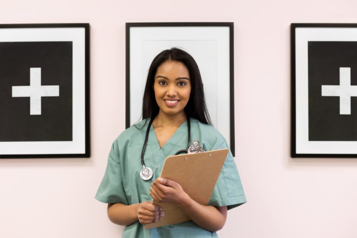 Registered Nurse holds a clipboard and wears green scrubs and a stethoscope