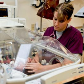 neonatal intensive care unit (nicu) nurse attends to a premature baby in an isolation chamber