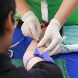 phlebotomist prepares to insert needle into patient's skin
