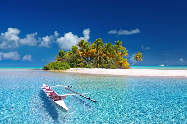 a small boat is moored near a beautiful tropical island with clear blue sea, palm trees and white sand beach