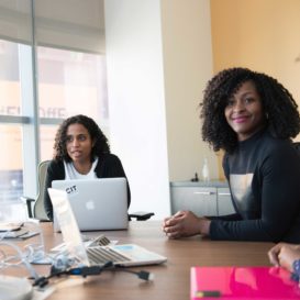 three women have a meeting at a conference room table with laptops