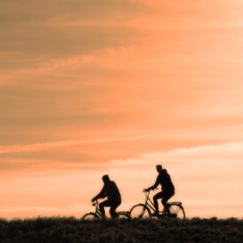 two cyclists riding against a peach sunset